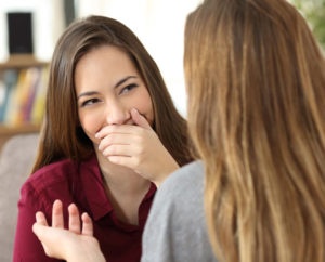 2 young women talking but one is covering her mouth with her hand because she has bad breath
