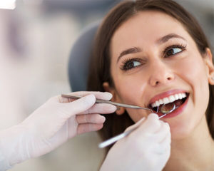 Dentist using mirror and pick cleaning inside of smiling mouth