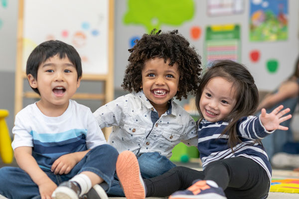 3 young children smile in a pre-k class