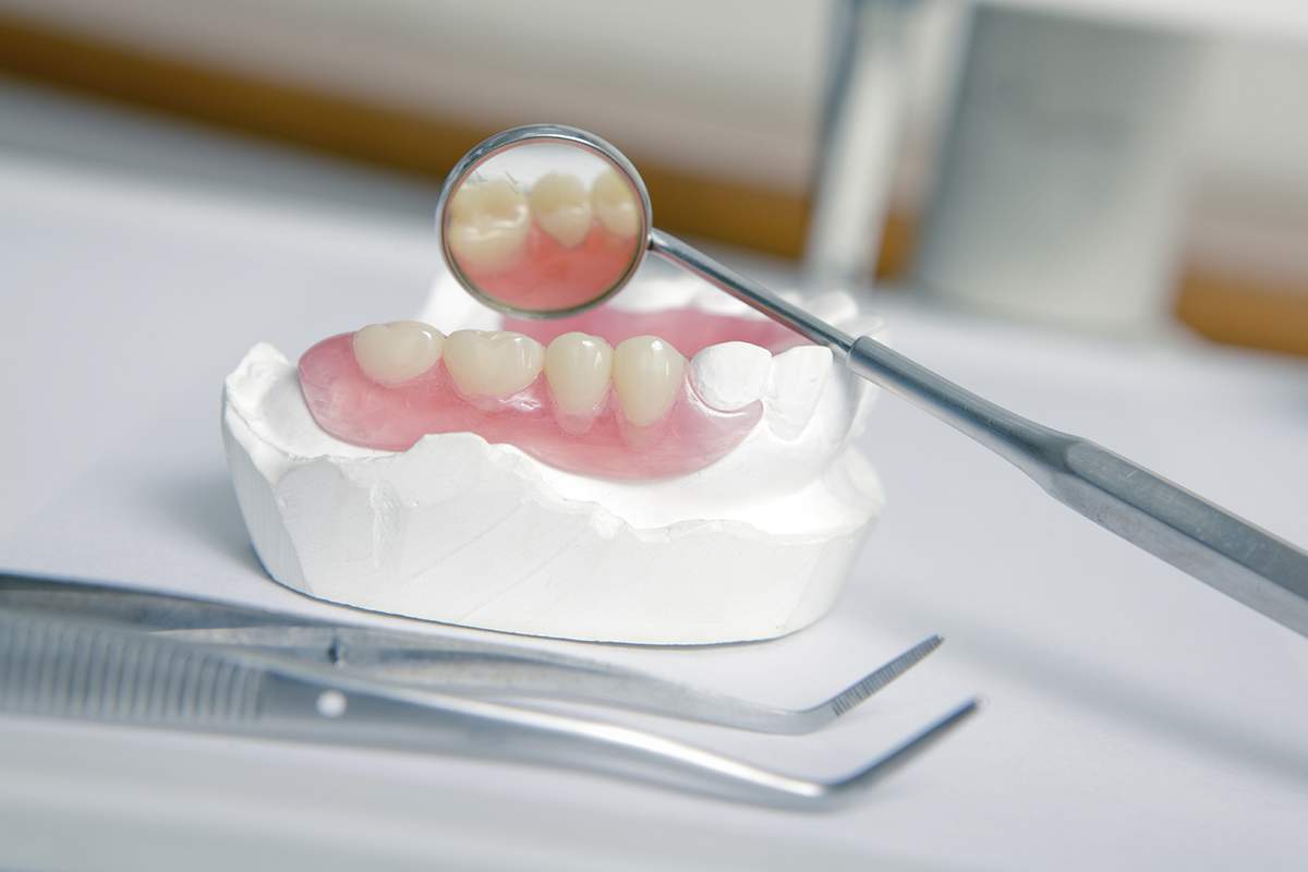 A dental model with artificial teeth and gums is shown. A mirror reflects the teeth, with tools nearby on a white surface.