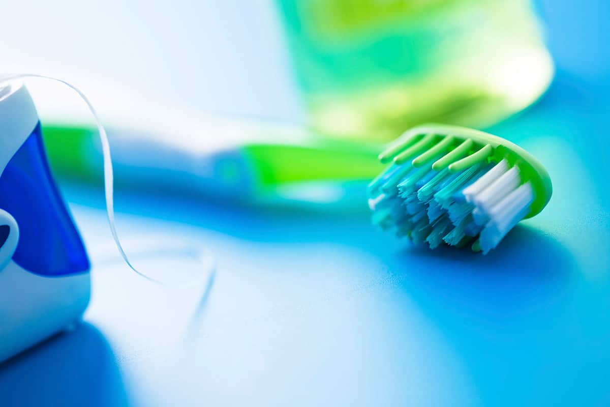 Close-up of a green and white toothbrush, dental floss, and a blurred bottle on a blue surface, representing dental hygiene.